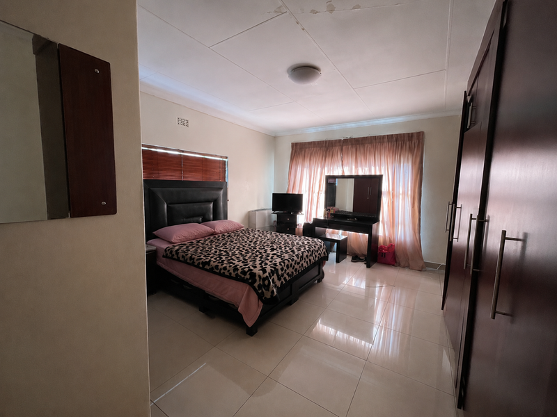 Spacious bedroom featuring tiled flooring, built-in cupboards, and large windows with curtains. Note visible water staining on the ceiling.