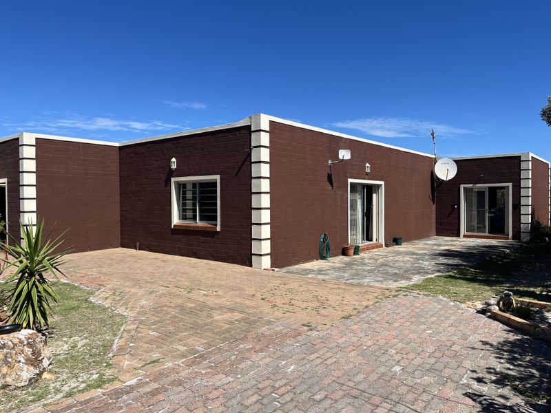 Rear exterior view of the house featuring a paved patio area, brick driveway, and sliding door access to the interior.