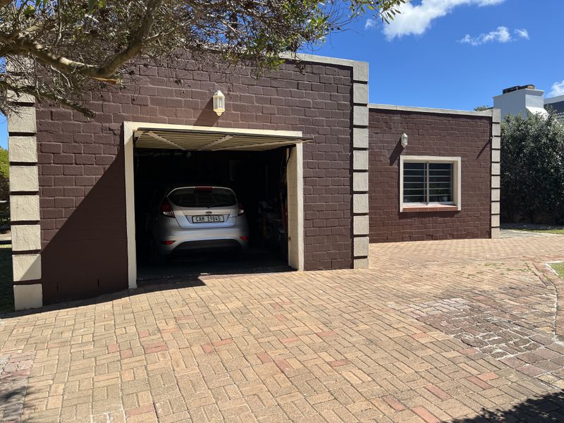 A detached garage featuring brown brickwork with contrasting corner quoins, a paved driveway, and secure window bars.