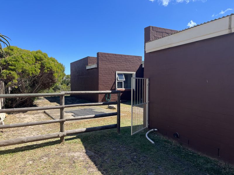 Rear exterior view of the property featuring painted masonry walls, a timber post and rail fence, and a small concrete patio area.