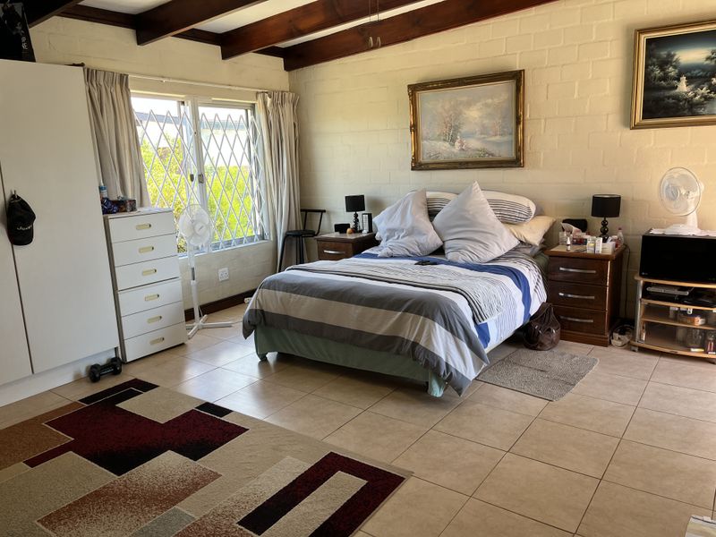 Spacious bedroom featuring exposed timber ceiling beams, tiled flooring, and painted brick walls with natural light from a sliding window.