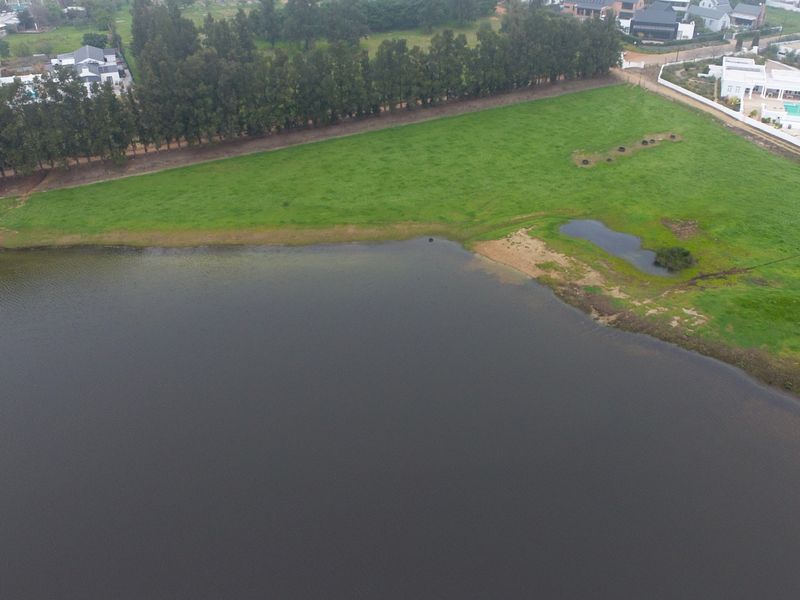 An aerial view of a vacant residential plot featuring expansive green land and direct waterfront access.