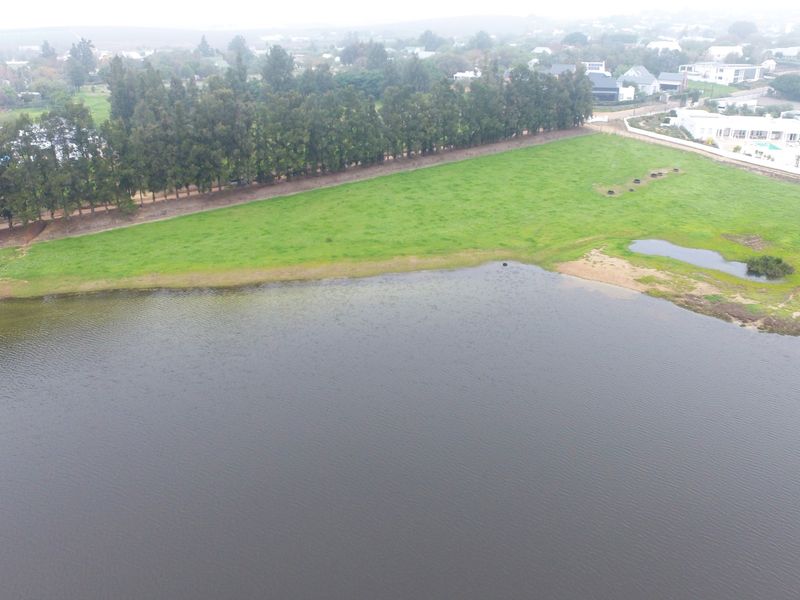 An aerial view of a vacant residential plot featuring direct waterfront access and established perimeter trees.