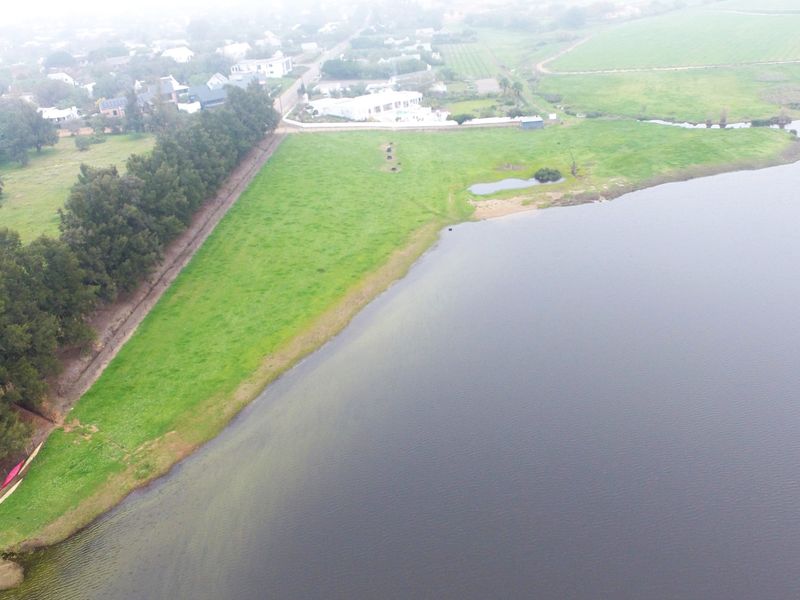 An aerial view of a vacant residential plot featuring expansive green land with direct waterfront access and mature tree lines.