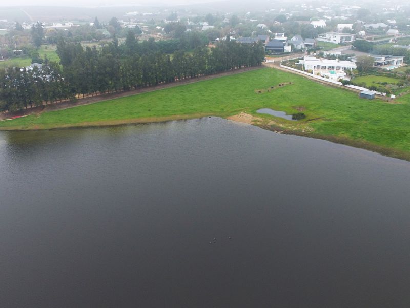 An aerial view of a vacant residential plot featuring expansive green land bordering a large body of water in a quiet neighborhood setting.