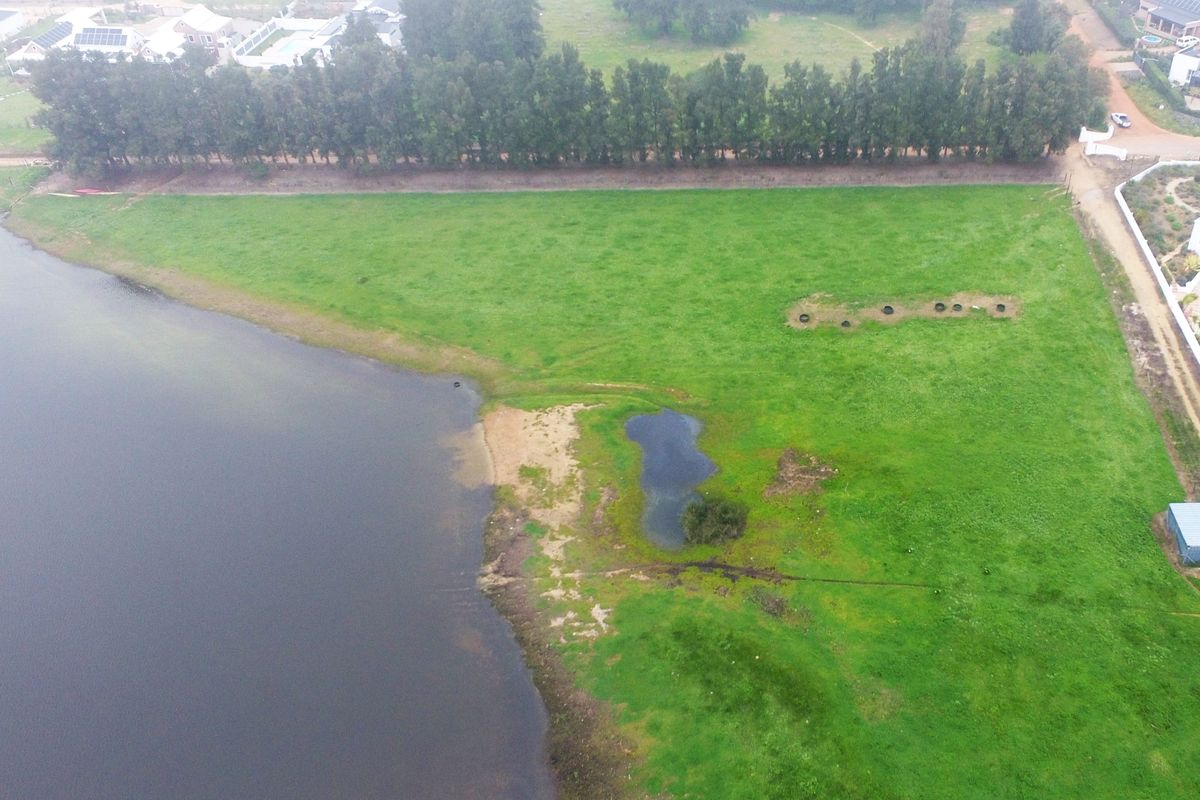 Aerial view of a vacant residential plot featuring direct waterfront access and expansive green space in a developed estate setting.