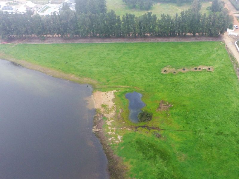 Aerial view of a vacant residential plot featuring direct waterfront access and expansive green space in a developed estate setting.