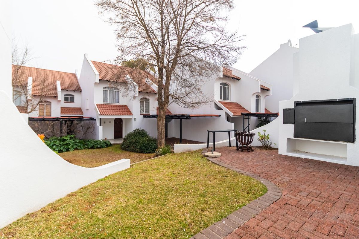 Rear view of the property featuring a paved patio area with a built-in braai, overlooking a small garden and the residential building facade.