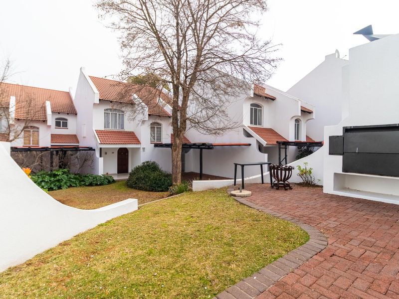 Rear view of the property featuring a paved patio area with a built-in braai, overlooking a small garden and the residential building facade.