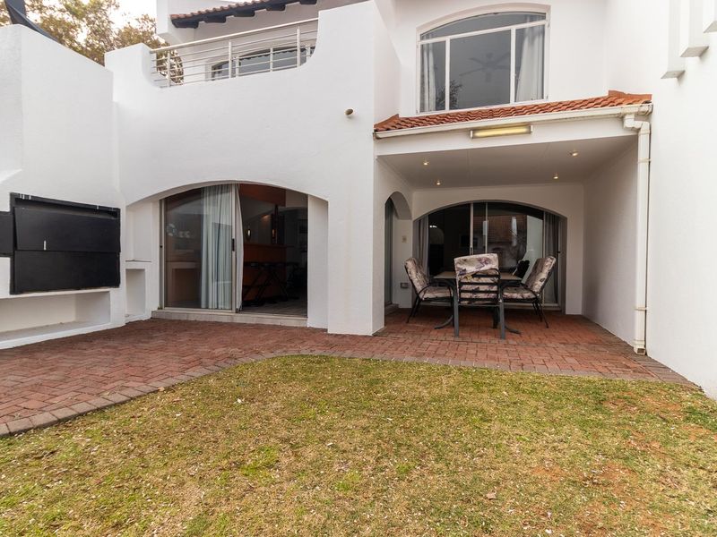 Rear exterior view featuring a covered patio, built-in braai, brick paved area, and access to the interior via sliding doors.