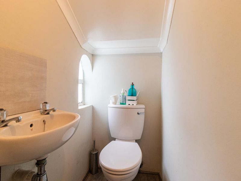 A compact guest bathroom featuring a pedestal basin, toilet, and a unique arched window, finished with simple coving.