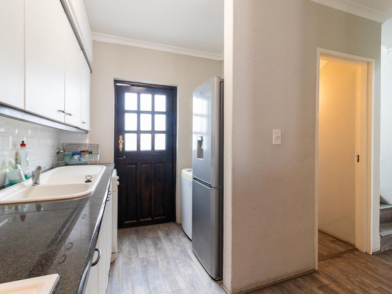 A functional scullery area featuring built-in cabinetry, a double sink with mixer tap, tiled splashback, and direct access to the exterior.