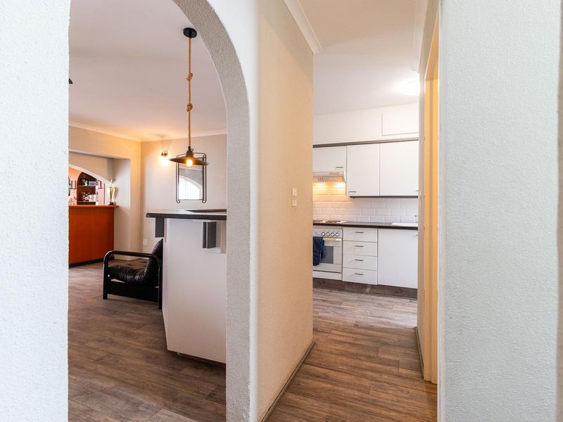 An open-plan living area featuring an arched entryway, a modern kitchen with white cabinetry, subway tile backsplash, and durable laminate flooring throughout.
