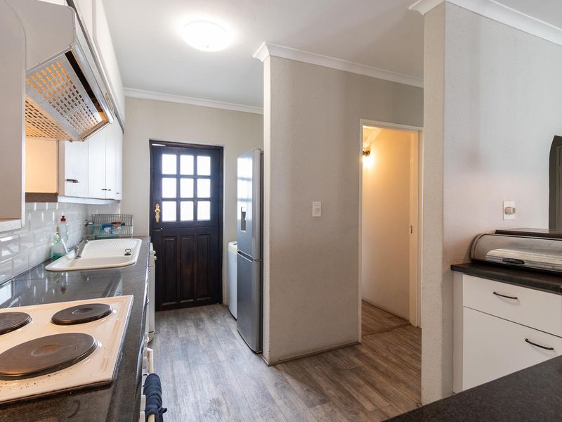 A functional kitchen featuring dark stone countertops, white cabinetry, an electric hob with extractor, and direct access to an exterior door.