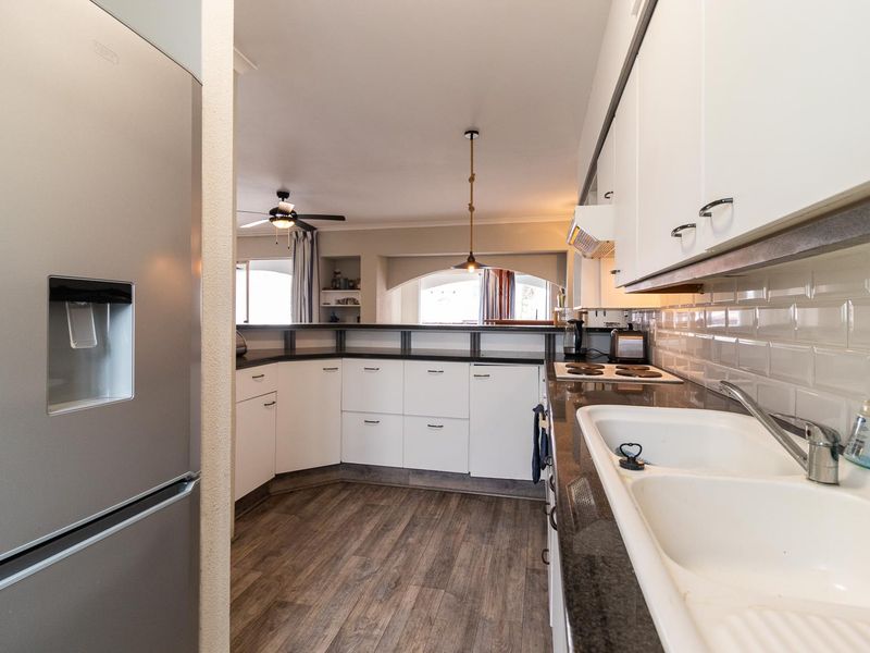 A functional kitchen featuring white cabinetry, dark stone countertops, a double basin sink, subway tile backsplash, and integrated electric cooktop with extractor fan.