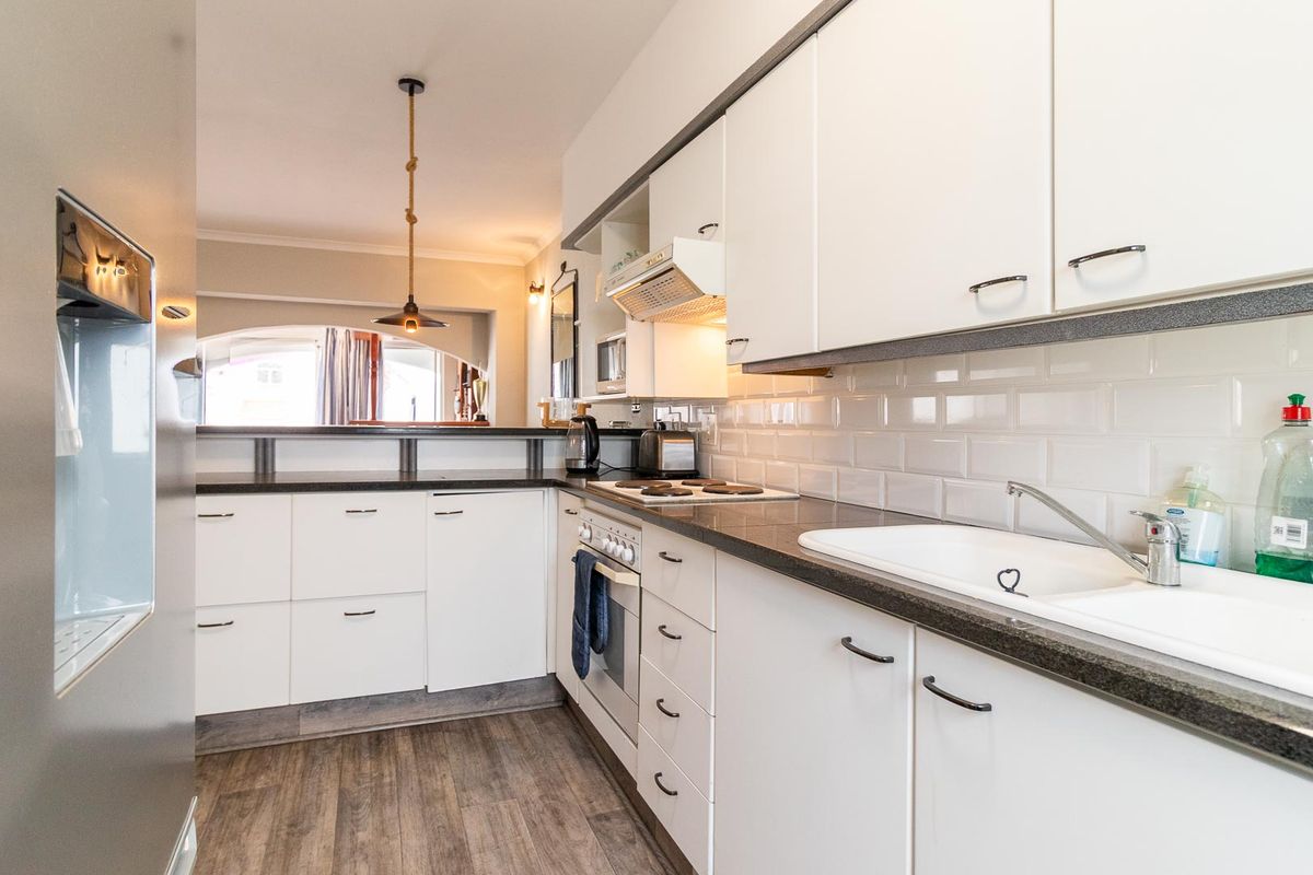 Modern kitchen featuring white cabinetry, dark stone countertops, subway tile backsplash, and integrated appliances with a breakfast bar overlooking the living area.