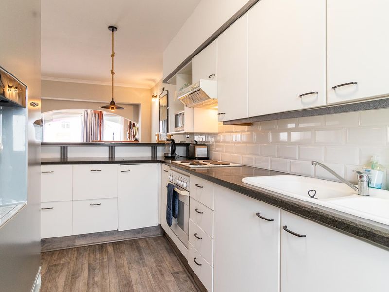 Modern kitchen featuring white cabinetry, dark stone countertops, subway tile backsplash, and integrated appliances with a breakfast bar overlooking the living area.