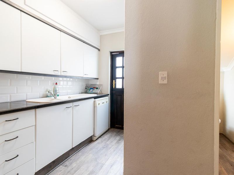 A functional scullery featuring white cabinetry, subway tile backsplash, dark laminate countertops, and direct access to the exterior via a timber door.