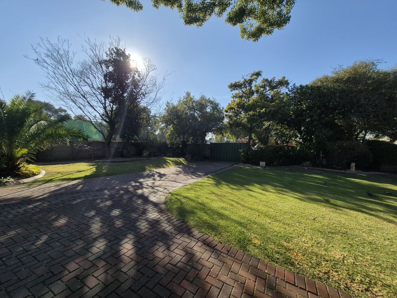A spacious backyard featuring a well-maintained lawn, mature trees, and a paved driveway area.