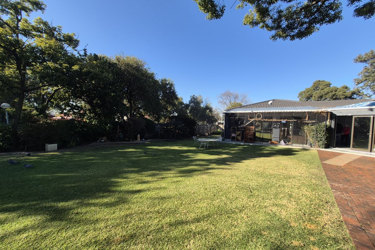 A spacious rear garden featuring a well-maintained lawn, mature trees, and a paved patio area adjacent to the house.