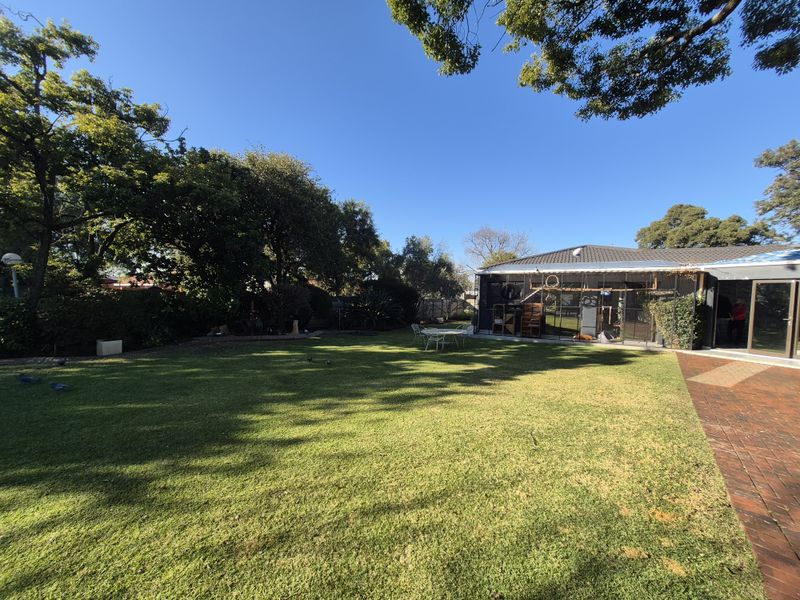 A spacious rear garden featuring a well-maintained lawn, mature trees, and a paved patio area adjacent to the house.