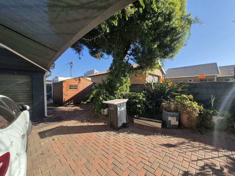 A paved rear courtyard area featuring a shade sail, a wooden garden shed, and perimeter boundary walling.