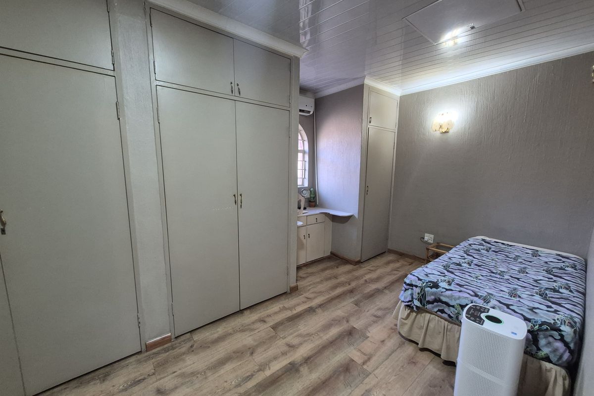 Bedroom featuring extensive built-in cupboard storage, laminate flooring, a built-in vanity area, and a wall-mounted air conditioning unit.