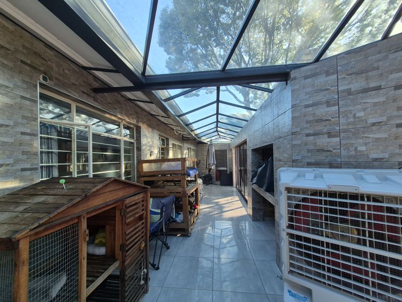 A spacious covered patio featuring a glass roof, tiled walls, and a built-in braai area, perfect for outdoor entertaining.