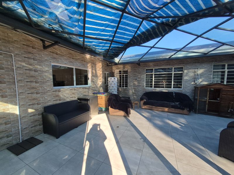 Covered outdoor patio area featuring stone-clad walls, large format floor tiles, and a protective metal-framed roof structure.
