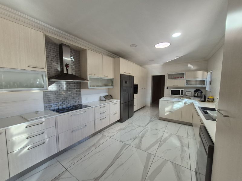 Modern kitchen featuring light wood cabinetry, stone countertops, subway tile backsplash, high-end integrated appliances, and large format marble-look porcelain floor tiles.