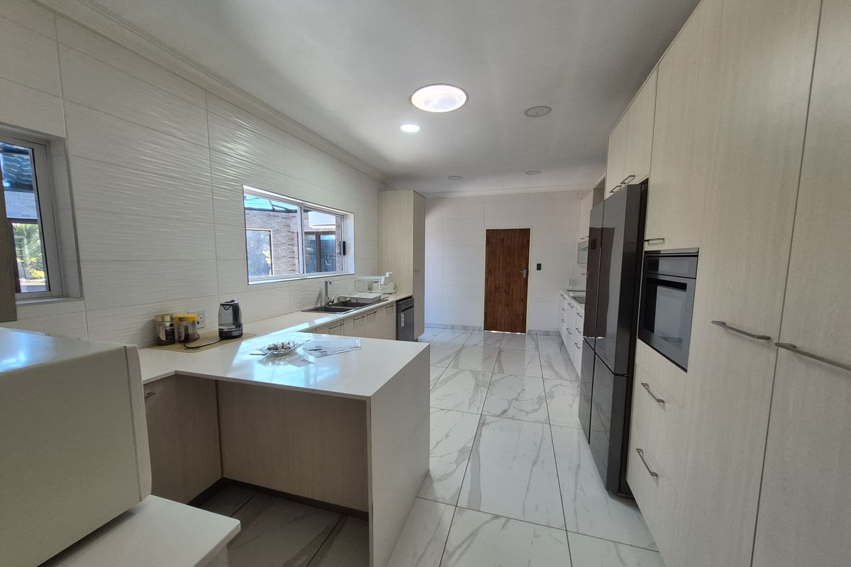 Modern kitchen featuring light wood-tone cabinetry, stone countertops, integrated oven, and large-format marble-look floor tiles with recessed lighting.