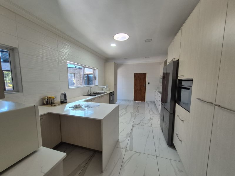 Modern kitchen featuring light wood-tone cabinetry, stone countertops, integrated oven, and large-format marble-look floor tiles with recessed lighting.