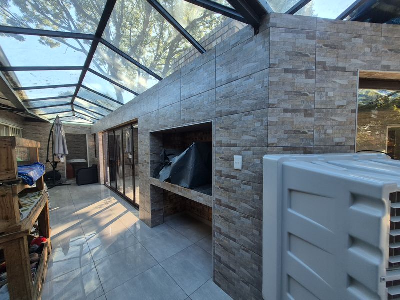 Covered patio area featuring a glass roof, tiled flooring, and a built-in braai, providing a bright and functional outdoor entertainment space.