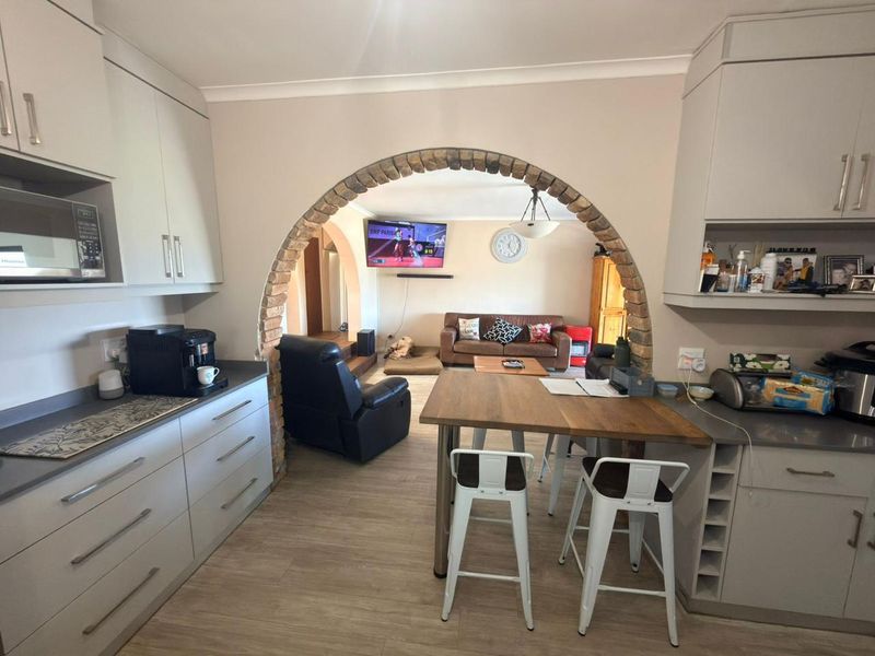 Open-plan kitchen and living area featuring a distinctive brick archway, modern cabinetry, and light laminate flooring, creating a connected and functional living space.