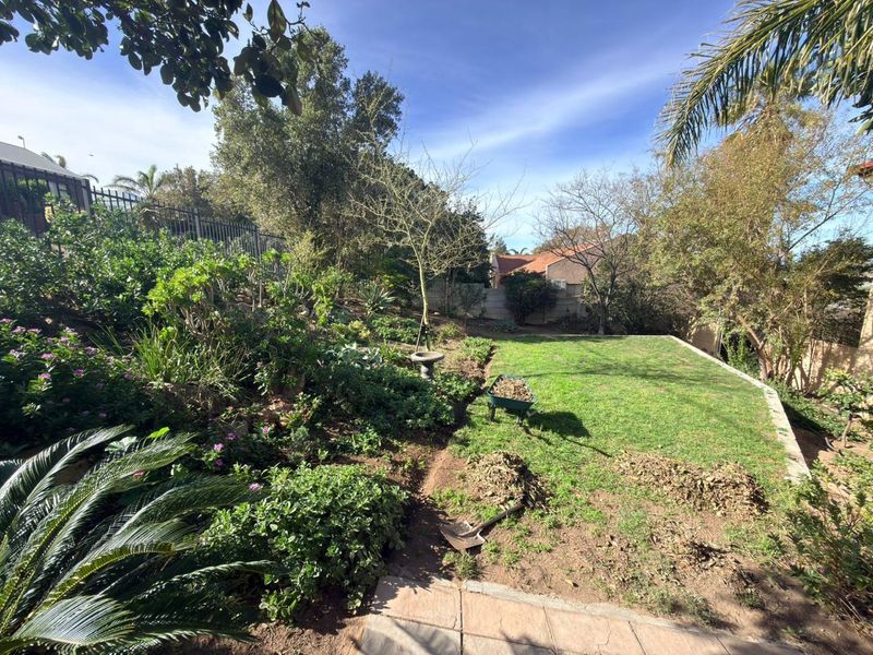 A spacious rear garden featuring a well-maintained lawn, established trees, and landscaped garden beds with boundary fencing.
