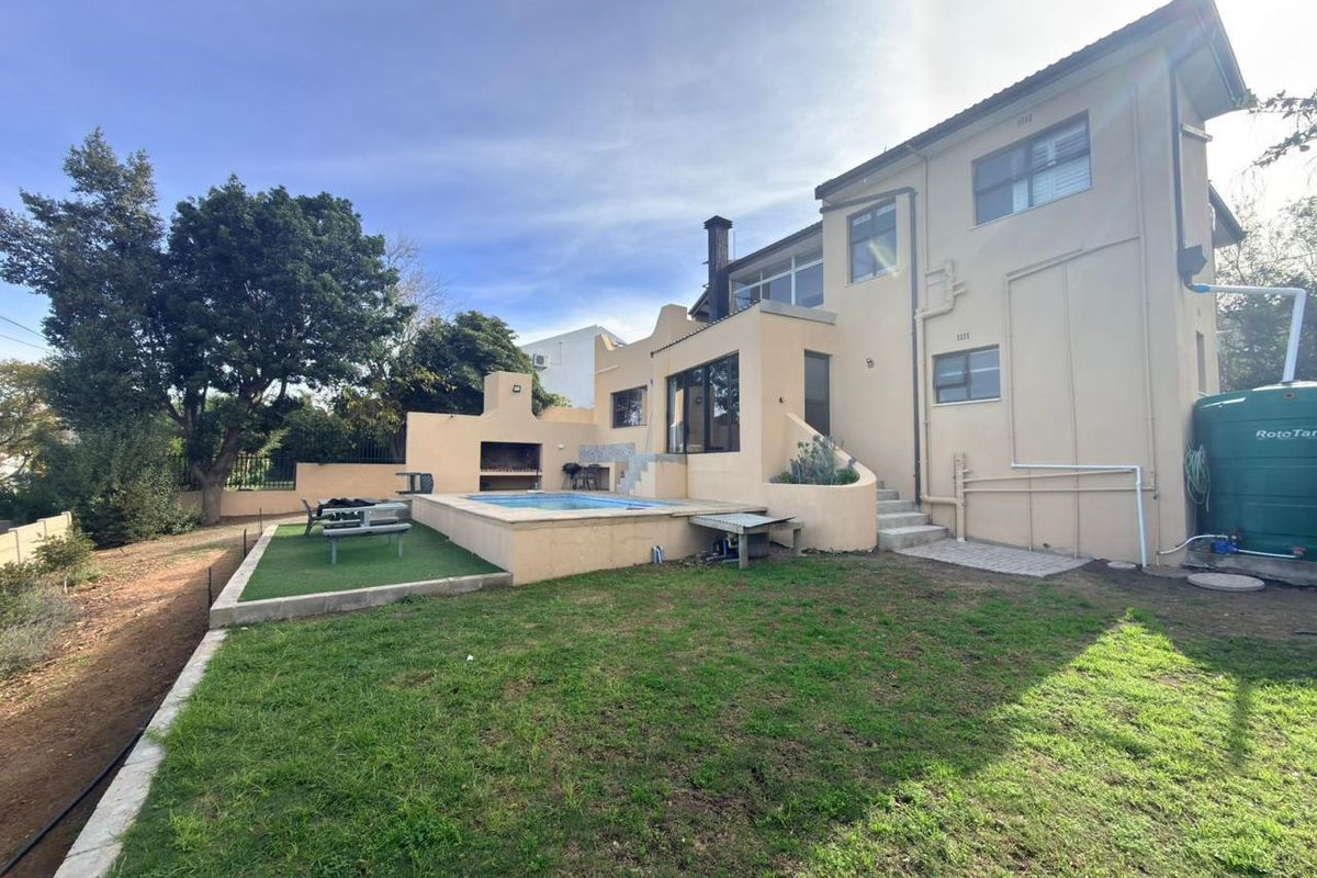 Rear exterior view featuring a swimming pool, built-in braai area, artificial lawn, and a water storage tank against the house facade.