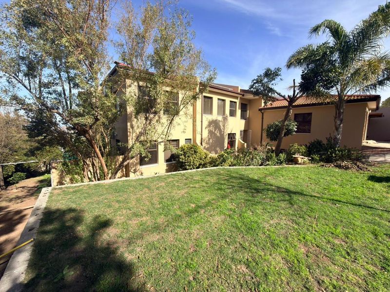 Rear view of the two-story house featuring a landscaped garden, retaining wall, and terracotta tiled roof.