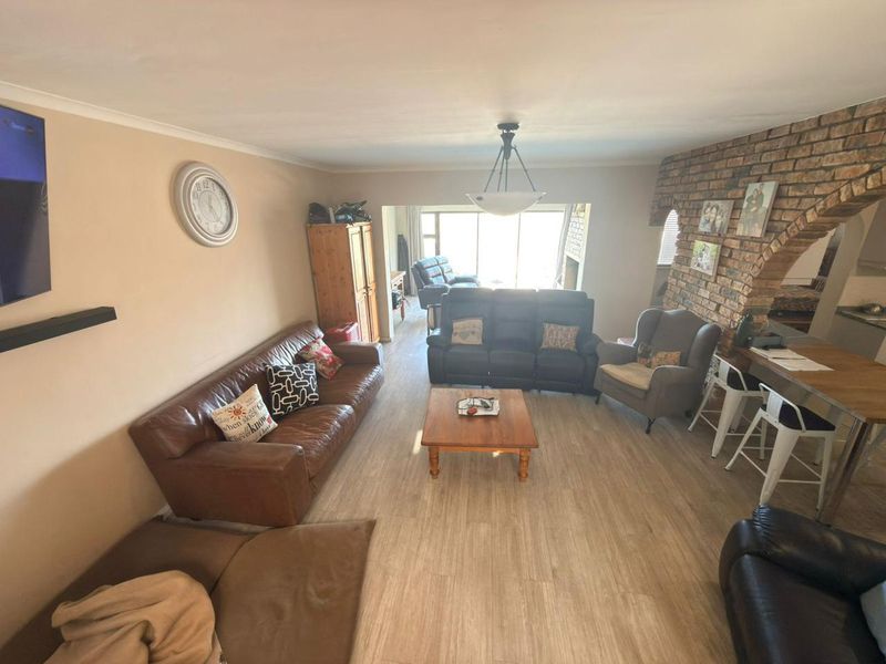 Spacious open-plan living area featuring light laminate flooring, an exposed brick feature wall with an archway, and neutral wall tones.