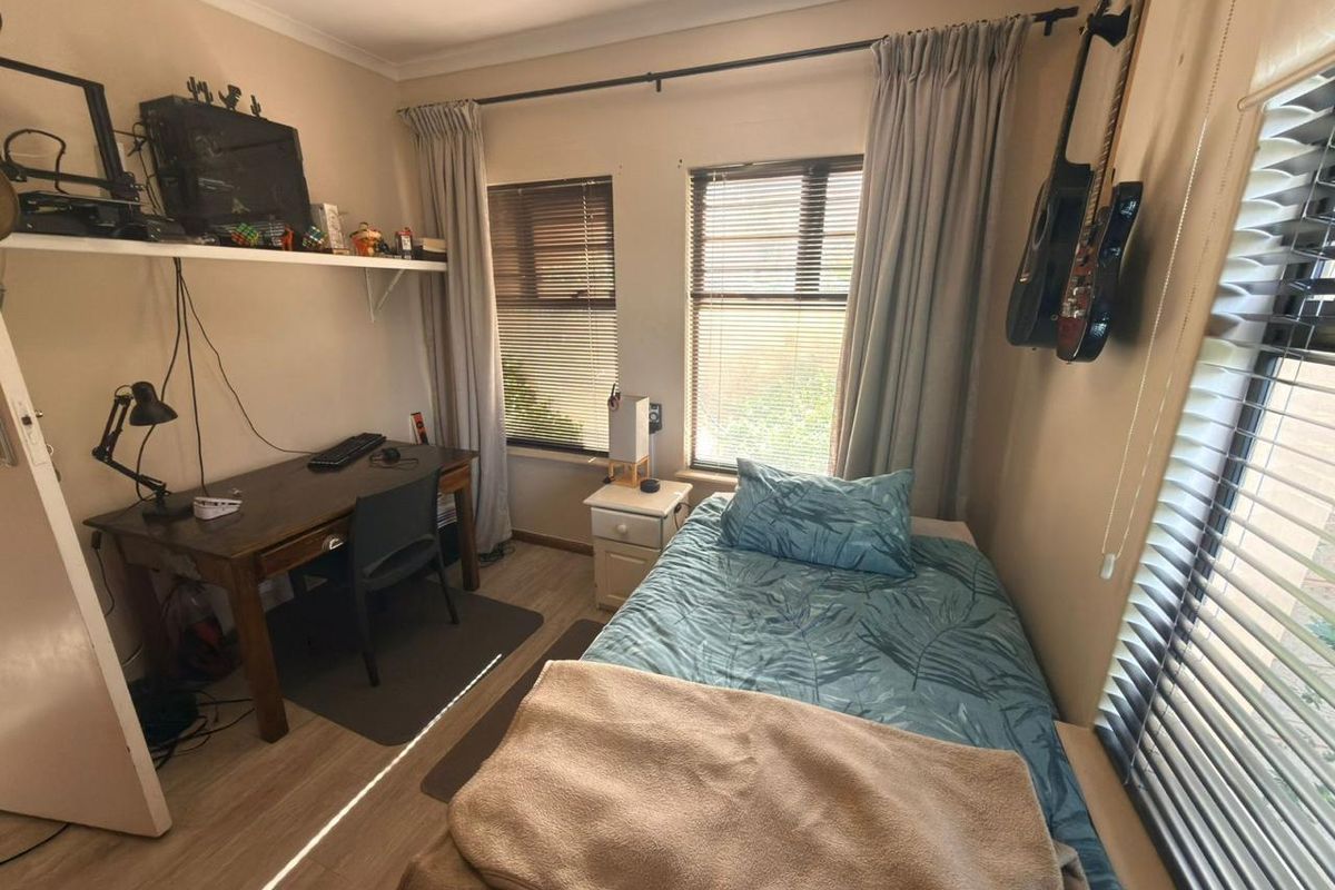 A compact bedroom featuring laminate flooring, dual windows with venetian blinds, and neutral wall finishes, suitable as a guest room or home office.