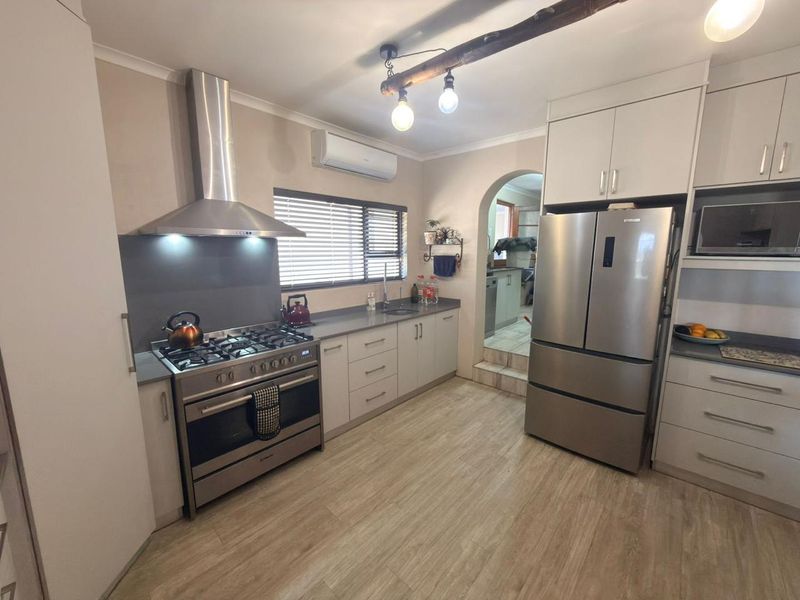 Modern kitchen featuring stainless steel gas stove, extractor fan, stone countertops, and ample built-in cabinetry with a convenient adjacent scullery area.