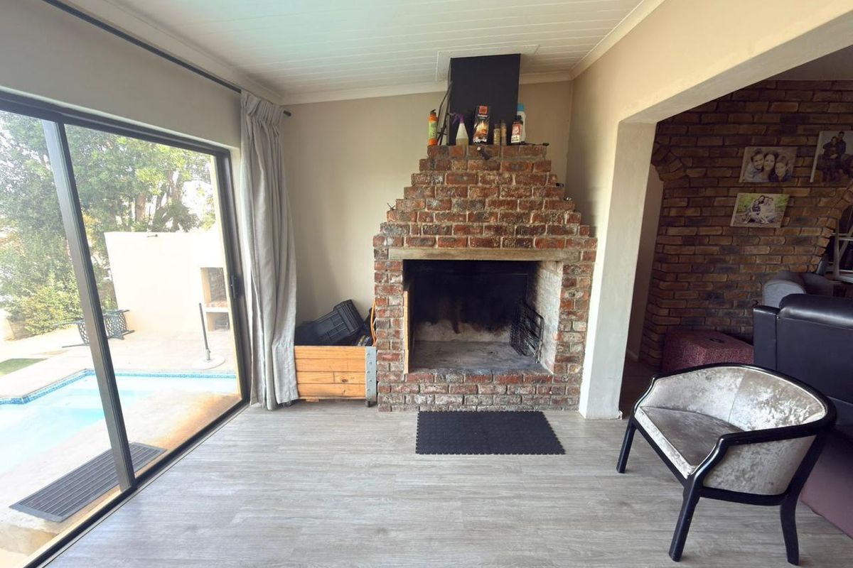 Living room featuring a prominent exposed brick fireplace, modern laminate flooring, and large sliding glass doors providing direct access to the pool area.