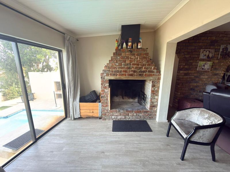Living room featuring a prominent exposed brick fireplace, modern laminate flooring, and large sliding glass doors providing direct access to the pool area.