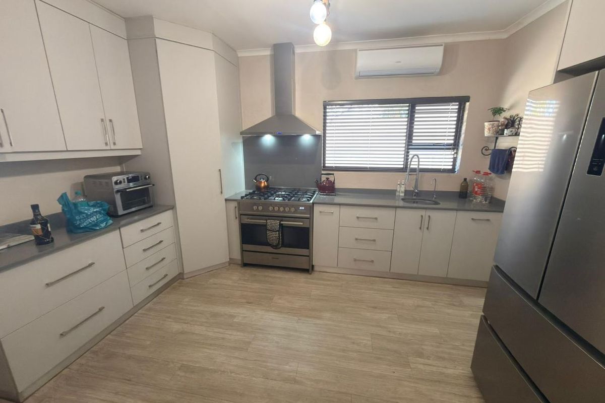 Modern kitchen featuring light-toned cabinetry, stainless steel gas stove with extractor fan, stone-look countertops, and durable laminate flooring.