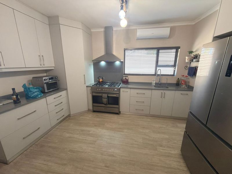 Modern kitchen featuring light-toned cabinetry, stainless steel gas stove with extractor fan, stone-look countertops, and durable laminate flooring.