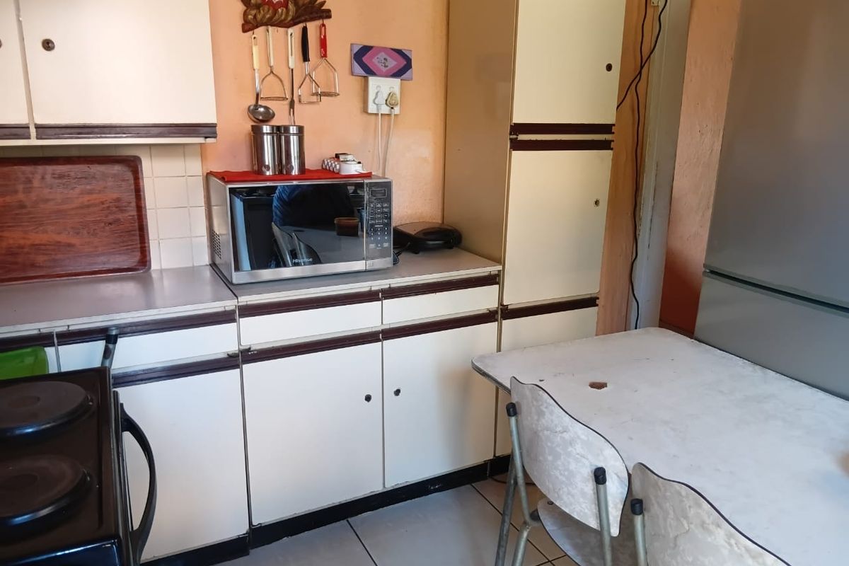 A dated kitchen featuring original built-in cabinetry, laminate countertops, and tiled flooring, offering significant potential for a modern renovation.