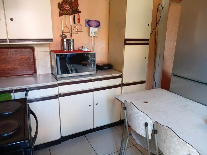 A dated kitchen featuring original built-in cabinetry, laminate countertops, and tiled flooring, offering significant potential for a modern renovation.