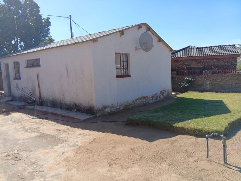 Rear view of a detached residential structure showing exterior wall deterioration and signs of rising damp, set within a basic garden area.