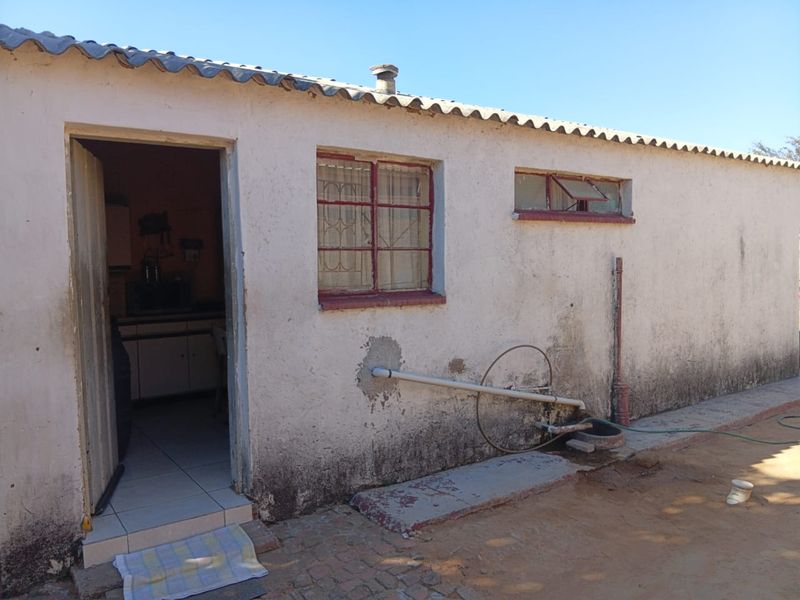 Rear exterior view of a basic dwelling showing weathered plaster, steel window frames, and external plumbing fixtures.
