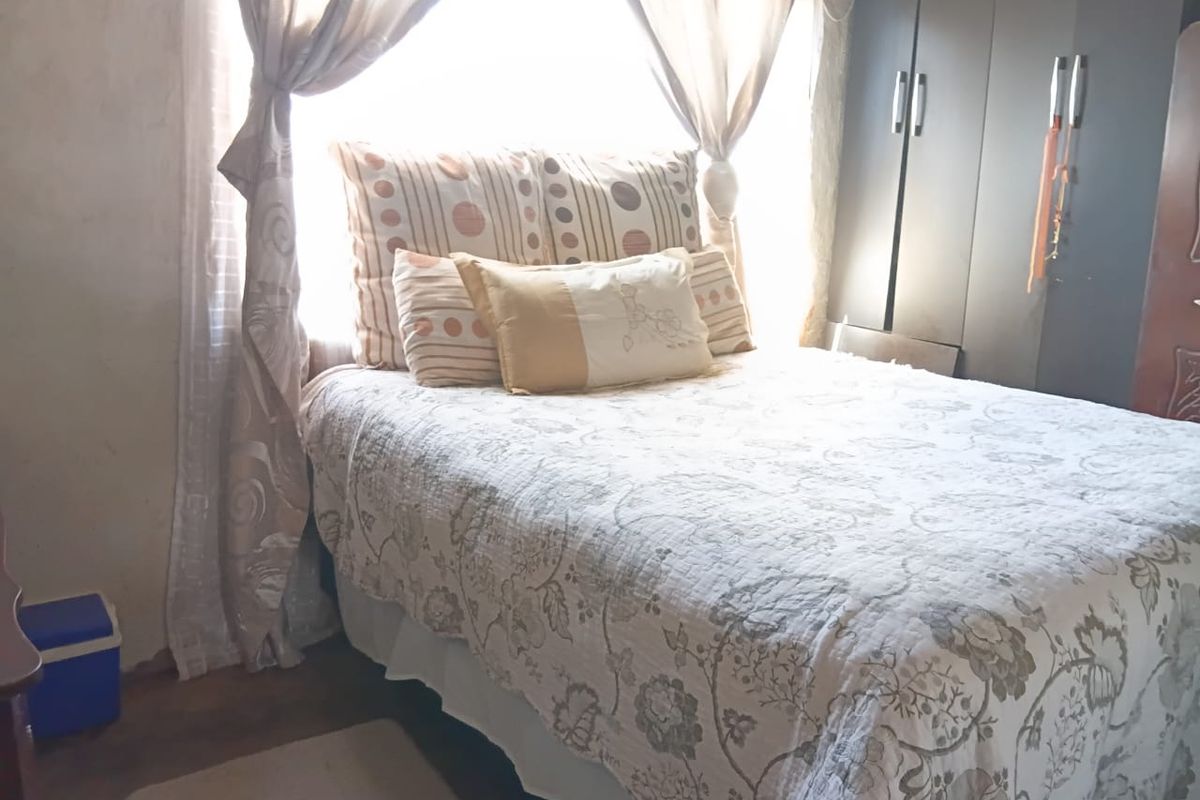 A bedroom featuring a built-in wardrobe and natural light from a large window, requiring cosmetic updates to the wall finishes.