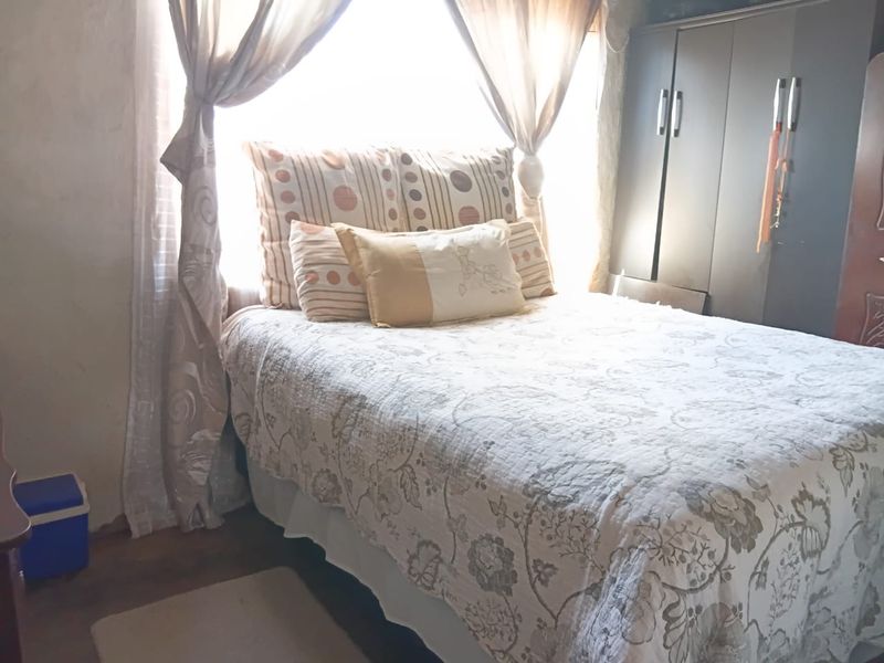 A bedroom featuring a built-in wardrobe and natural light from a large window, requiring cosmetic updates to the wall finishes.